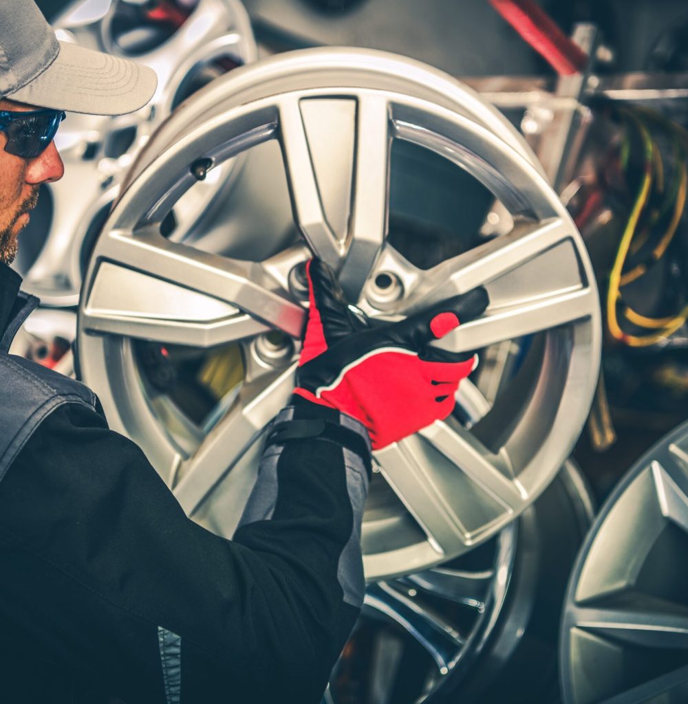 Buying New Alloy Wheels and Seasonal Tires Change Concept Photo. Caucasian Car Service Worker with Large Rim in Hands.